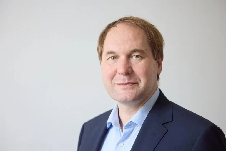 Eine Wissenschaftlerin und ein Wissenschaftler arbeiten hinter einer Glasfassade und mischen Chemikalien mit Großgeräten.